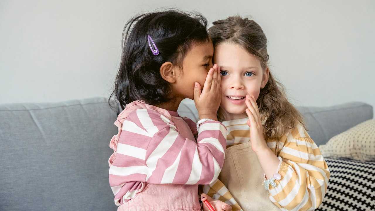 Two girls are whispering to each other.