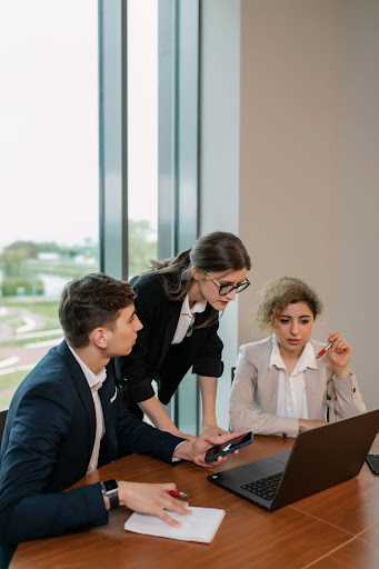 Three formally dressed colleagues discussing infront of a laptop.