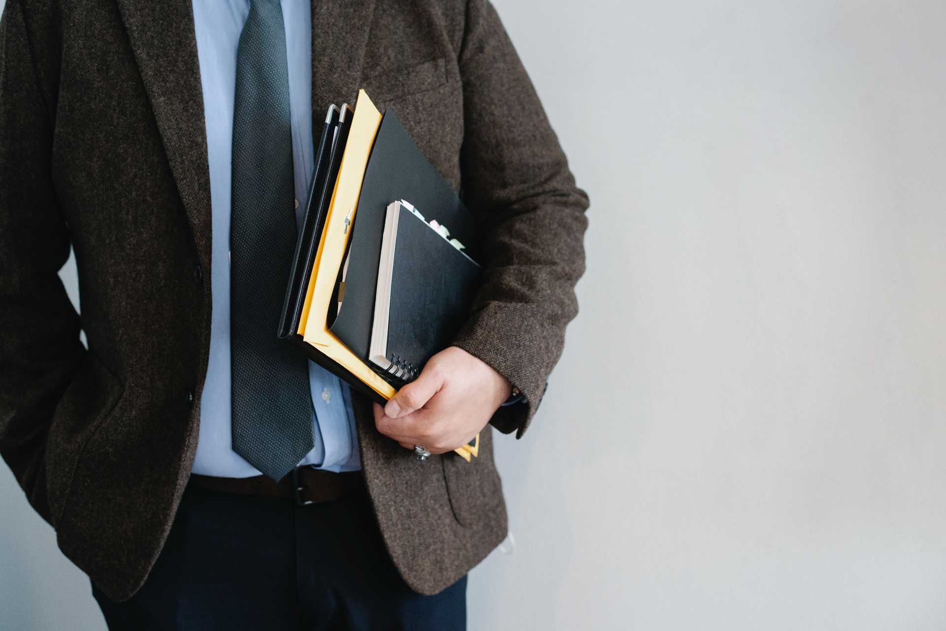 Image of a businessman in a suite carrying folders with paperwork.